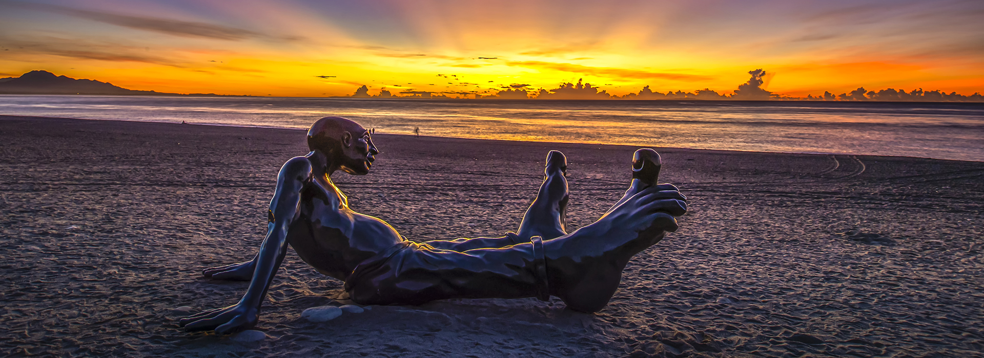 海岸邊的人型藝術裝置與遠方的霞光